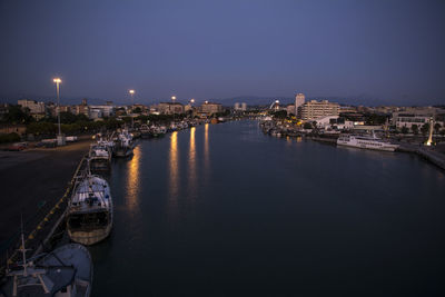 Illuminated city by river against sky at night