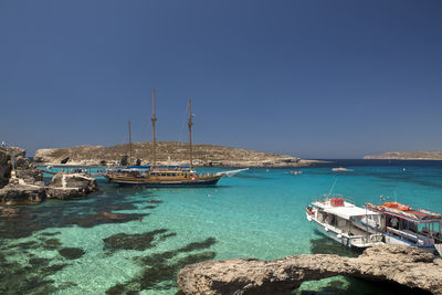 Boats moored on sea against clear blue sky