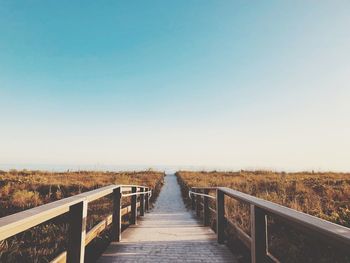 Footbridge along landscape against clear sky