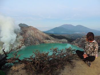 Woman sitting on mountain against sky