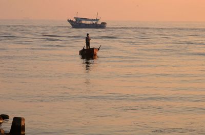 Men in sea against sky during sunset