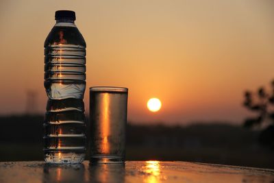 Close-up of water bottle on table against sky during sunset