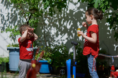 Siblings are playing with soap bubbles in the backyard on a sunny day