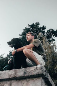 Low angle view of woman sitting with dog against sky