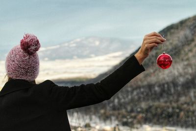 Rear view of woman holding red bauble on mountain during winter