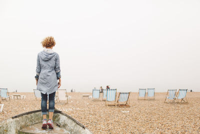 Rear view of woman standing on boat moored at beach against clear sky