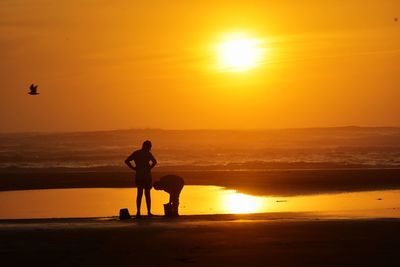 Silhouette man on beach against sky during sunset