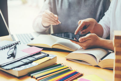 Midsection of students with digital tablet studying on desk