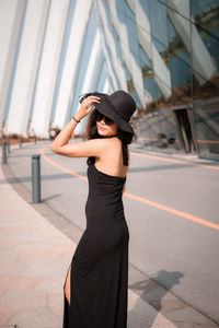 Portrait of woman wearing hat while standing on footpath