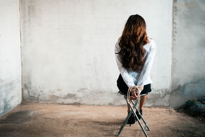 Rear view of woman with tied hands sitting on chair 