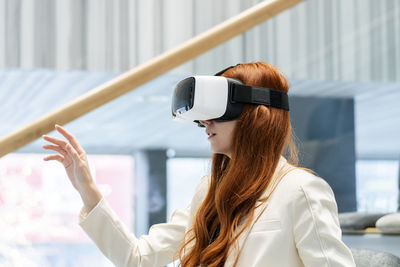 Redhead working woman wearing virtual reality headset gesturing in office