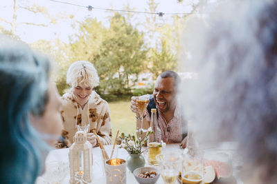 Happy gay friends laughing while having drinks with friends during dinner party in back yard