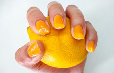 Close-up of hand holding orange slice over white background