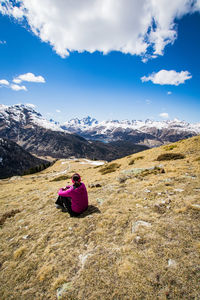 Rear view of woman sitting on snowcapped mountain against sky