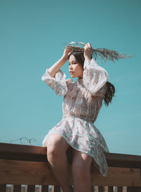 Low angle view of young woman against blue sky