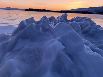 Snow covered land and sea against sky during sunset