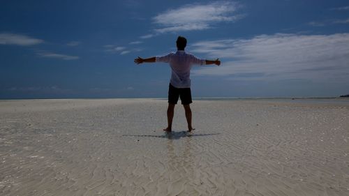 Rear view of man with arms outstretched standing at beach