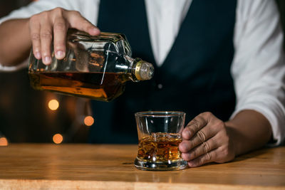 Midsection of man pouring wine in glass on table