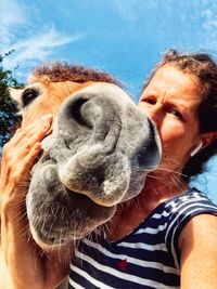 Low angle portrait of woman kissing horse against sky