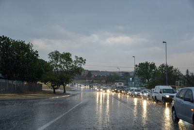 Wet road by trees against sky during rainy season