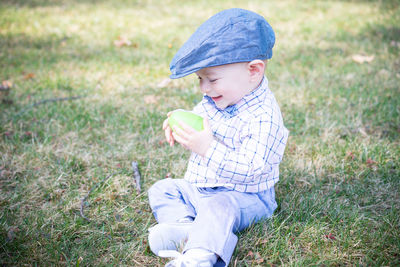 Full length of baby boy holding easter egg while sitting on field