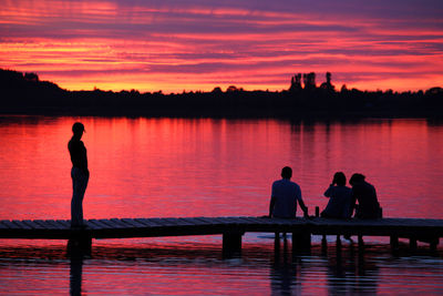 Silhouette people on pier over lake during sunset