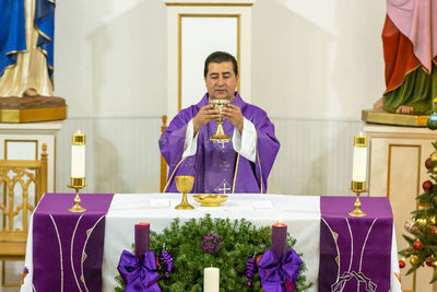 Priest holding wine while standing at table in church