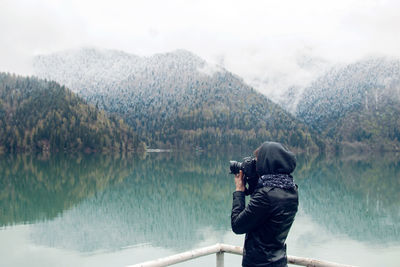 Woman in a leather jacket with a camera taking pictures ritsa lake in the spring morning