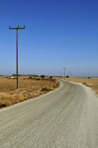 Road by electricity pylon against clear sky