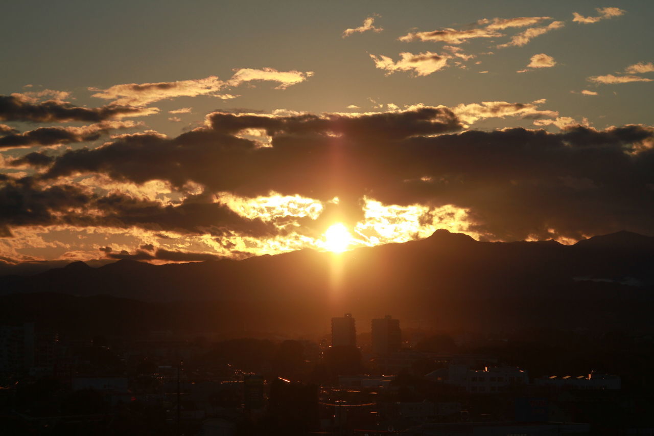 sunset, sun, sky, sunbeam, cloud - sky, building exterior, sunlight, scenics, silhouette, built structure, architecture, beauty in nature, cityscape, mountain, city, cloud, orange color, nature, lens flare, tranquil scene