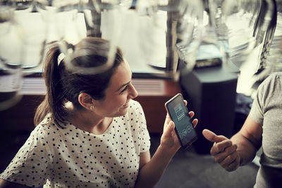 High angle view of smiling female showing smart phone to male partner in cafe