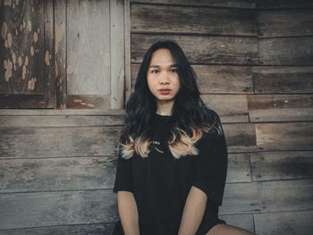 Portrait of beautiful young woman standing against wood