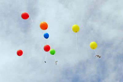 Low angle view of colorful balloons flying against cloudy sky