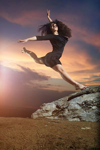 Young woman jumping on rock against sky during sunset