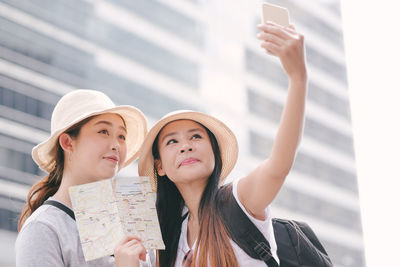Woman holding map while friend taking selfie