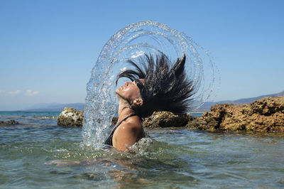 Young man splashing water in sea against clear sky