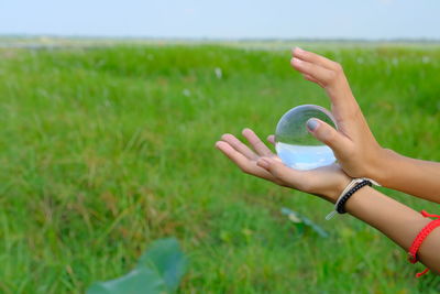 Cropped hands holding crystal ball on grassy land
