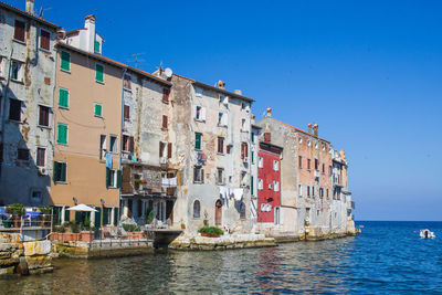 Buildings by sea against clear blue sky