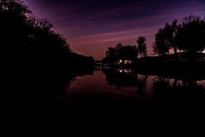 Silhouette trees by lake against sky at night