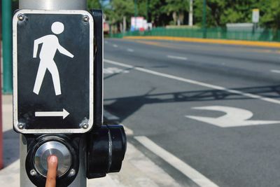 Cropped finger of person pressing button below crossing sign