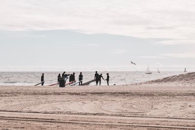 People with surfboard at beach against sky