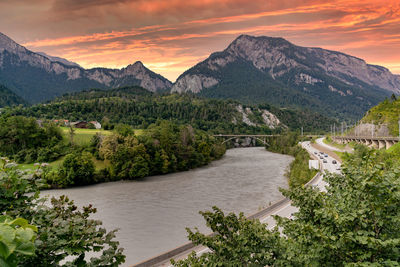 Scenic view of river and mountains against sky at sunset