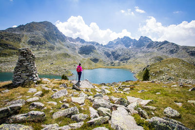 Rear view of woman standing on rock by lake against sky