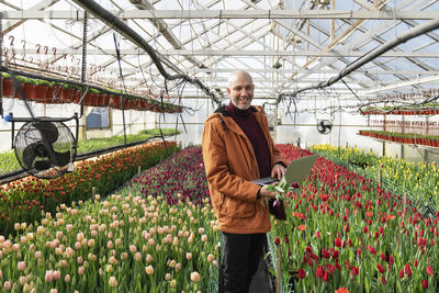 Smiling businessman with laptop amidst tulip flowers in greenhouse