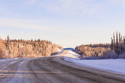 Road amidst snow covered landscape against sky