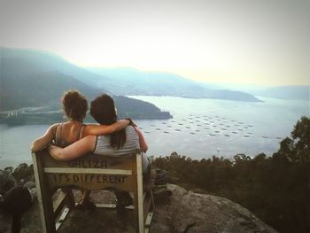 Rear view of couple sitting on chair by lake