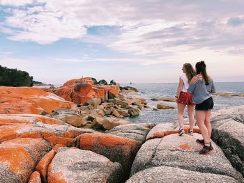 Woman standing on rock by sea against sky