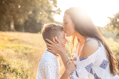 Mother kissing on son forehead in sunny day