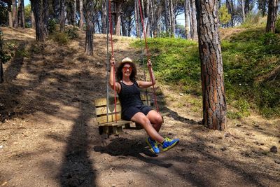 Full length portrait of woman sitting on swing in forest