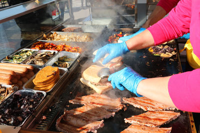 Chef with blue gloves and cooked sausages in the hot plate of a stand of street food